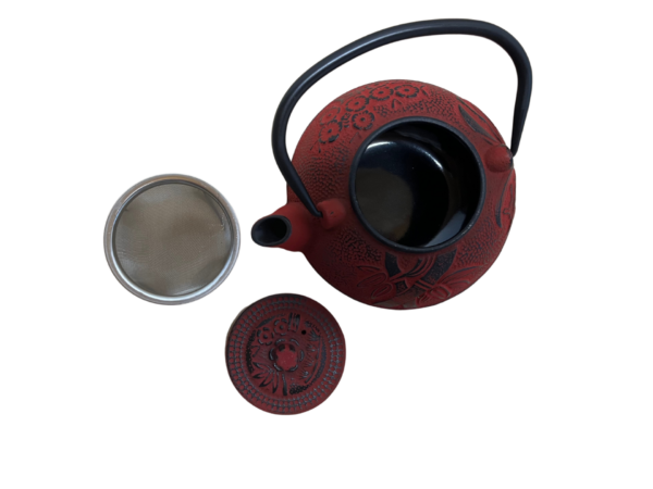 Liatinový čajník v červenej farbe a uškom s vybratým sitkom a vrchnáčikom z vrchnej strany