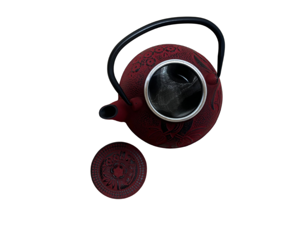 Liatinový čajník v červenej farbe a uškom otvorený so sitkom vnútri